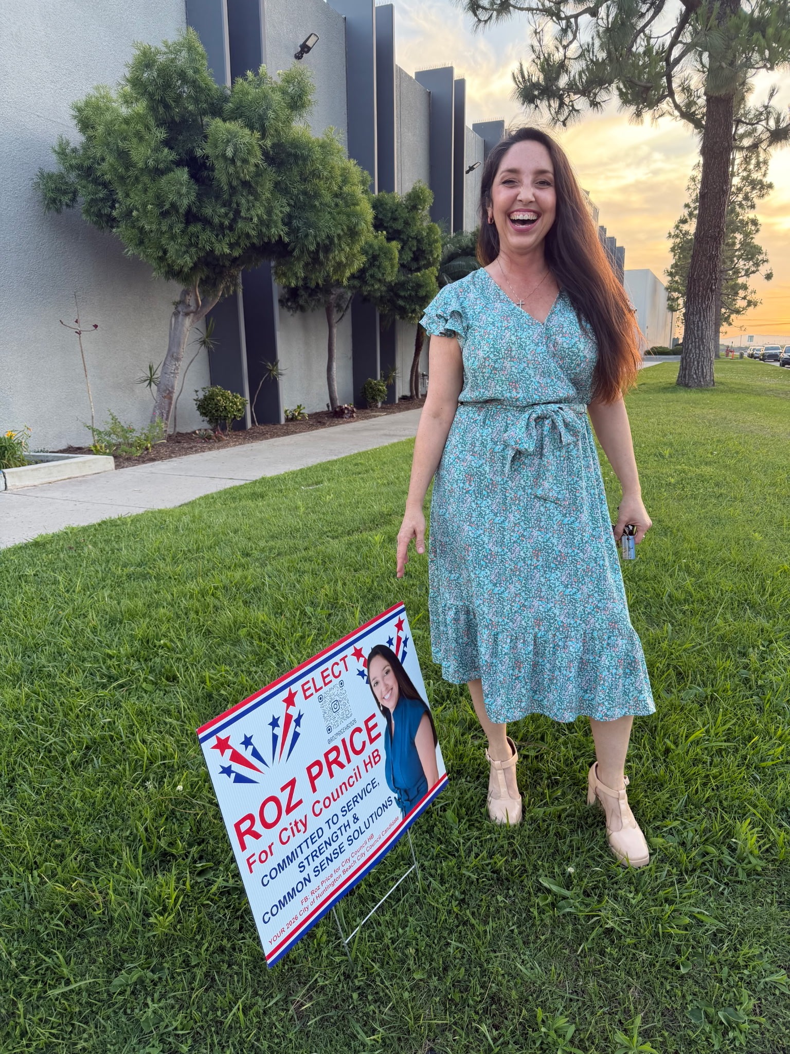 Roz Price standing with campaign yard sign at sunset